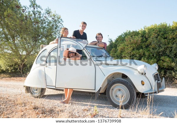Group of happy people near a car in summertime,\
retro style.