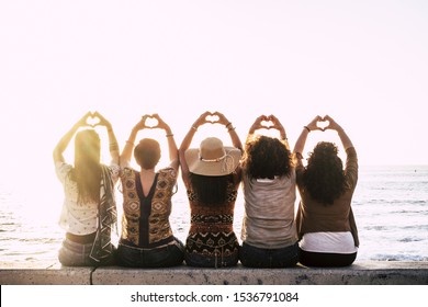 Group of happy people  outdoor friends women viewed from back doing love hearth sign with up hands - concept of relationship - sunset and sea in background