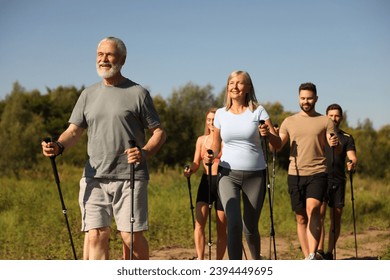 Group of happy people practicing Nordic walking with poles outdoors on sunny day - Powered by Shutterstock