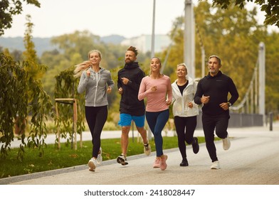 Group of happy people in sportswear jogging together in the park. friends running outdoor having sport training in nature. Team of runners at morning workout. Sport, fitness lifestyle concept. - Powered by Shutterstock