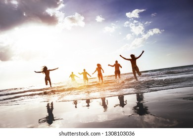 Group Of Happy Peoples Runs And Jumps At Sunset Sea Beach. Tropical Tourism Concept