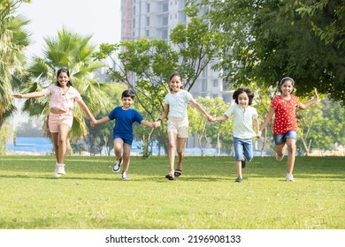 Group of happy playful Indian children holding each other hands running together outdoors in spring park. Asian kids Playing in garden. Summer camp background.  - Powered by Shutterstock