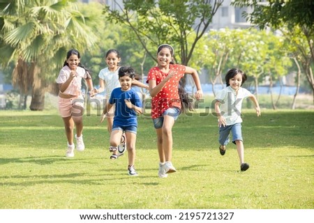 Group of happy playful Indian children running outdoors in spring park. Asian kids Playing in garden. Summer holidays. 