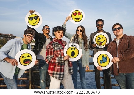 Group of happy positive friends holding discs with handdrawn emoji smiley faces standing outdoors looking at the camera - social network marketing team portrait