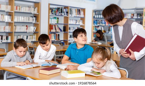 Group of happy school kids studying in school library with friendly female teacher