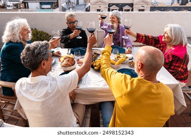 Group of happy senior friends bonding at home for dinner party - Cheerful and youthful old mature multiethnic people having fun and dining on a rooftop terrace  - Powered by Shutterstock