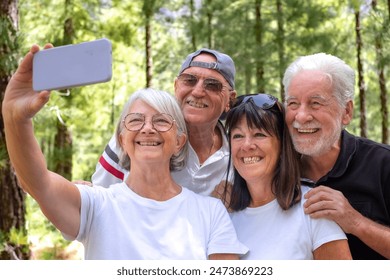 Group of happy senior friends enjoying a trekking day in the forest, elderly caucasian retirees smiling carefree take selfie with smartphone, healthy lifestyle in outdoors concept - Powered by Shutterstock