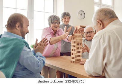 Group of happy senior people having fun and playing board games in retirement home. Several cheerful old men and women gather around table and take turns to take wood blocks out of wooden tower - Powered by Shutterstock