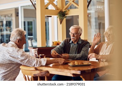 Group Of Happy Senior People Playing Cards On Patio At Nursing Home.