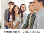 Group of a happy smiling friends high school students in casual clothes standing together and looking cheerful and positively at the camera in hallway. Portrait of friendly guys and girls indoors.