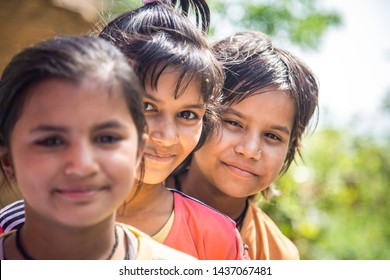 Group of happy smiling Indian little village girls standing in front of mud house.