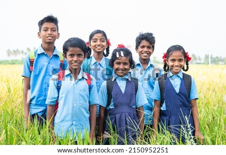 group of happy smiling village school kids in uniform standing at middle paddy field by looking camera - concept of friendship, education and togetherness
