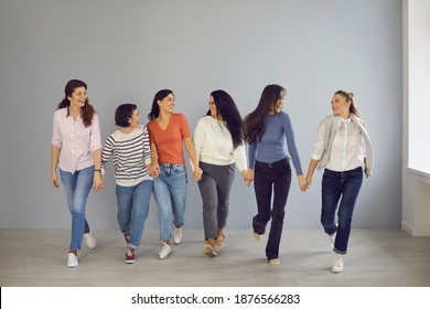 Group Of Happy Smiling Young Women In Their 20s And 30s Walking Hand In Hand In Modern Office Or Studio. Concept Of Gathering Together, Mutual Support, Female Solidarity, And Confidence In Future