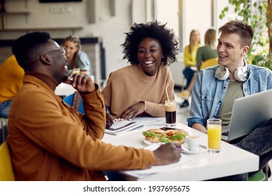 Group of happy students talking while studying at university cafeteria. Focus is on black female student. 