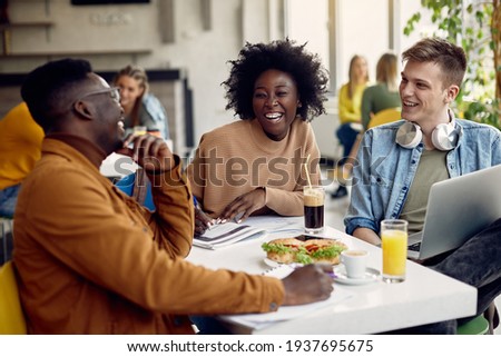 Group of happy students talking while studying at university cafeteria. Focus is on black female student. 