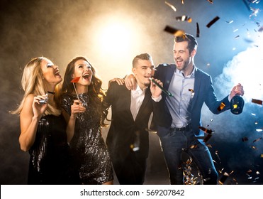 Group of happy stylish friends celebrating with champagne bottle and confetti