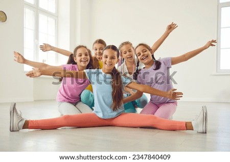 Group happy successful joyful flexible children kid girls in sportswear sit on floor after lesson at sport dance school gymnastic hall recreation club circus studio, spread arms, smile, look at camera