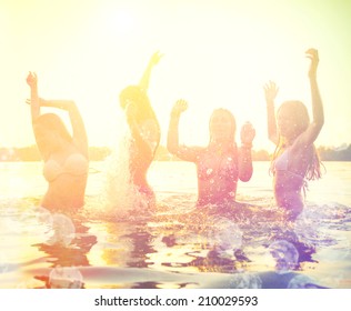 Group Of Happy Teen Girls Playing In Water At The Beach On Sunset. Beauty And Joyful Teenager Friends Having Fun, Dancing And Spraying Over Summer Sunset. Beach Party. Sun Flare.