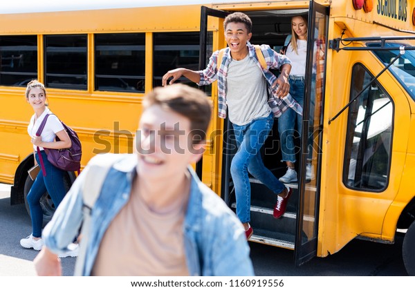group of\
happy teen scholars running out school bus\
