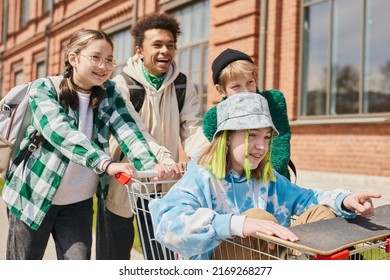 Group Of Happy Teens Having Fun Outdoors Rolling Girl In Shopping Cart