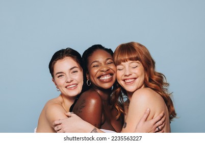 Group of happy women with different skin tones smiling and embracing each other. Three diverse women feeling comfortable in their natural skin. Body positive young women standing together in a studio.