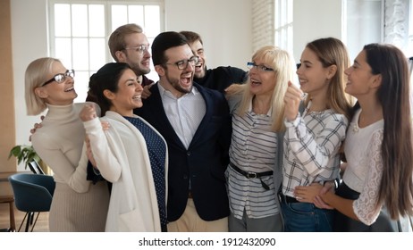 Group Of Happy Workers Of Different Generations Hugging Like Family Together, Laughing. Excited Diverse Business Team Cheer Celebrating Success. Corporate Achievement, Win, Teamwork, Community Concept