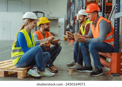 Group of happy workers, managers wearing hard hats, vests, holding lunch boxes, eating lunch, sitting, talking to each other during break. Concept of lunch together - Powered by Shutterstock