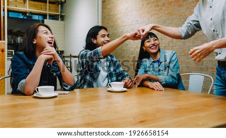 Group of happy young Asia friends having fun a great time and greeting with friendship fist pump while sitting together at cafe restaurant. Coffee shop holiday activity, friendship lifestyle concept.
