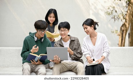 Group of happy young Asian college students sitting on a bench, looking at a laptop screen, discussing and brainstorming on their school project together. - Shutterstock ID 2298328405
