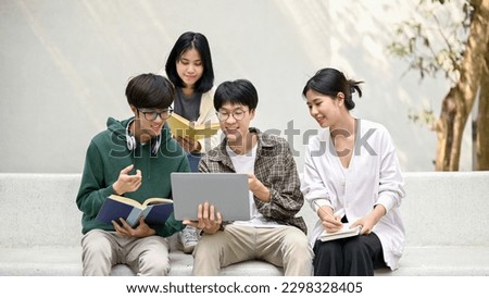 Group of happy young Asian college students sitting on a bench, looking at a laptop screen, discussing and brainstorming on their school project together.