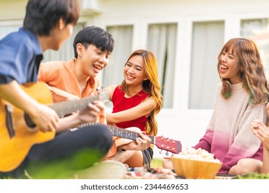 Group of Happy young Asian man and woman friends enjoy and fun reunion meeting party at home backyard with playing guitar, singing, eating food and drinking beer together on summer holiday vacation. - Powered by Shutterstock