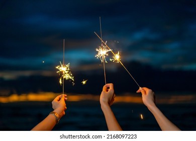 Group of Happy young Asian woman sitting and playing sparklers together on tropical island beach at summer night. Smiling female friends enjoy and fun outdoor lifestyle on holiday travel vacation trip