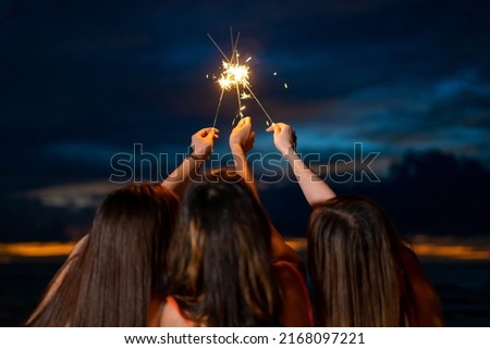 Group of Happy young Asian woman sitting and playing sparklers together on tropical island beach at summer night. Smiling female friends enjoy and fun outdoor lifestyle on holiday travel vacation trip