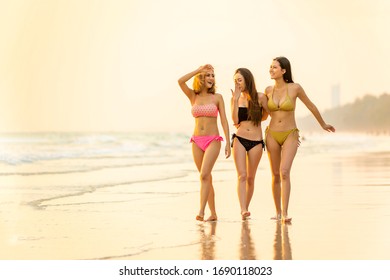 Group of Happy young beautiful Asian women in bikini swimwear walking and smiling together on the beach at sunset. Three sexy girls friends relax and having fun in summer holidays vacation travel.