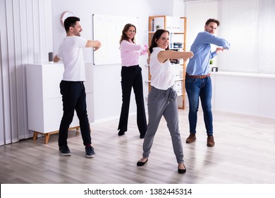 Group Of Happy Young Businesspeople Doing Stretching Exercise In Office