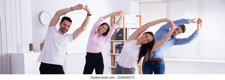 Group Of Happy Young Businesspeople Doing Stretching Exercise In Office