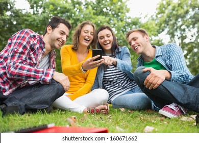 Group Of Happy Young College Students Looking At Mobile Phone In The Park