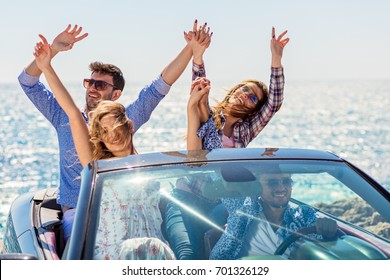 Group of happy young friends in cabriolet with raised hands driving on sunset - Powered by Shutterstock