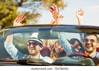 Group of happy young friends in cabriolet with raised hands driving on sunset - Powered by Shutterstock