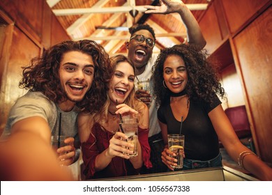 Group of happy young friends with drinks gathered for party in club. Excited men and woman with drinks taking selfie during party. - Powered by Shutterstock