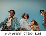 Group of happy young friends having fun outdoors, enjoying sunny day under blue sky. Joyful Gen Z people embracing friendship and laughter.