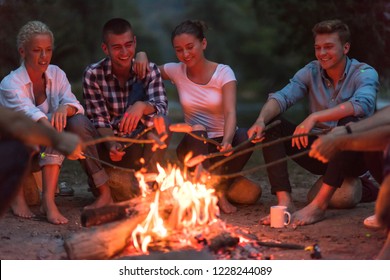 a group of happy young friends relaxing and enjoying  summer evening around campfire on the river bank - Powered by Shutterstock