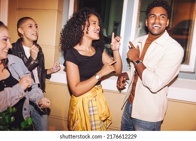 Group of happy young friends singing and dancing to their favourite song outdoors. Multicultural young people having a good time while hanging out together on a weekend night.