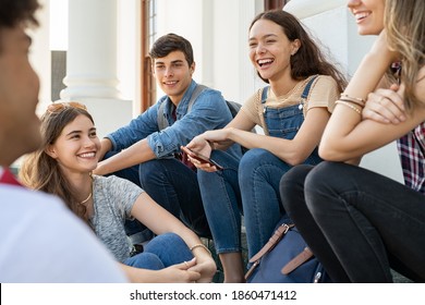 Group of happy young friends sitting in college campus and talking. Cheerful group of  smiling girls and guys feeling relaxed after university exam. Excited millenials laughing and having fun outdoor. - Shutterstock ID 1860471412