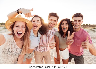 Group of happy young friends in summer clothes taking a selfie while standing at the beach - Powered by Shutterstock