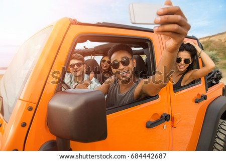 Group of happy young friends taking a selfie while sitting in a convertible car outdoors
