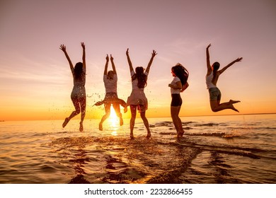 Group of happy young girls are having fun and jumping at sunset beach - Powered by Shutterstock