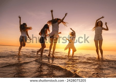 Group of happy young girls are having fun and dancing at sunset sea beach