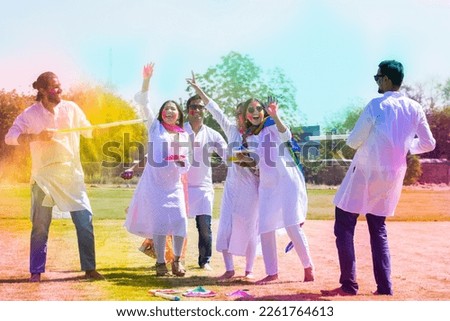 Group of happy young Indian friends celebrating holi festival at park outdoor, Playful adult men and women with colorful paint faces playing with gulal.