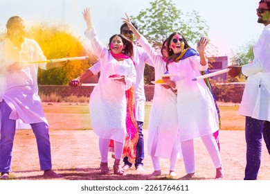 Group of happy young Indian people celebrating holi festival at park outdoor, Playful guys and girls with colorful paint faces playing with gulal.